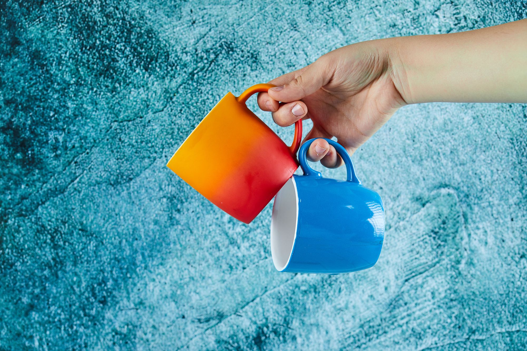 hand-holding-two-mugs-blue-background_1755687952325.jpg